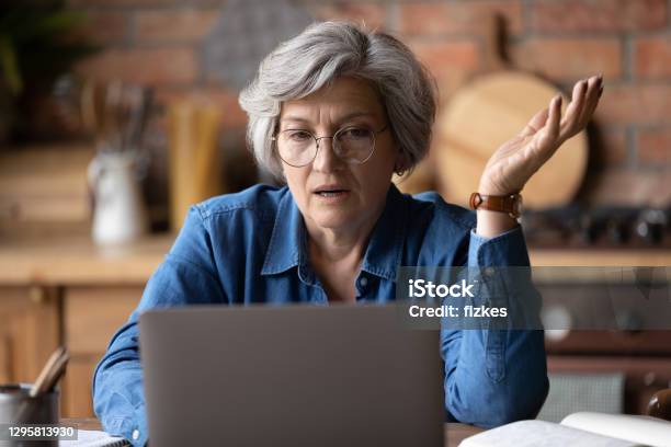 Confused Middle Aged Woman In Glasses Looking At Computer Screen Stock Photo - Download Image Now