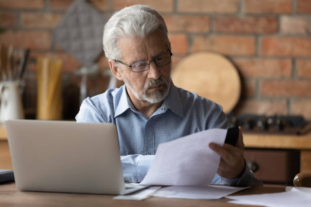 istock Focused middle aged man doing financial paperwork at home. 1295813952
