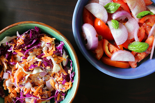 Photo showing blue dishes of homemade coleslaw and tomato salad, made with chopped tomatoes, shredded red cabbage, grated carrot and slices of mild Spanish sliced onion, mixed with a generous amount of low-calorie mayonnaise.