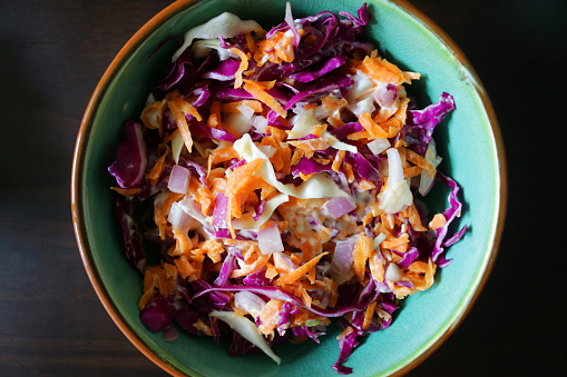 Photo showing elevated view of turquoise dish of homemade coleslaw, made with shredded red cabbage, grated carrot and slices of mild Spanish sliced onion, mixed with a generous amount of low-calorie mayonnaise.