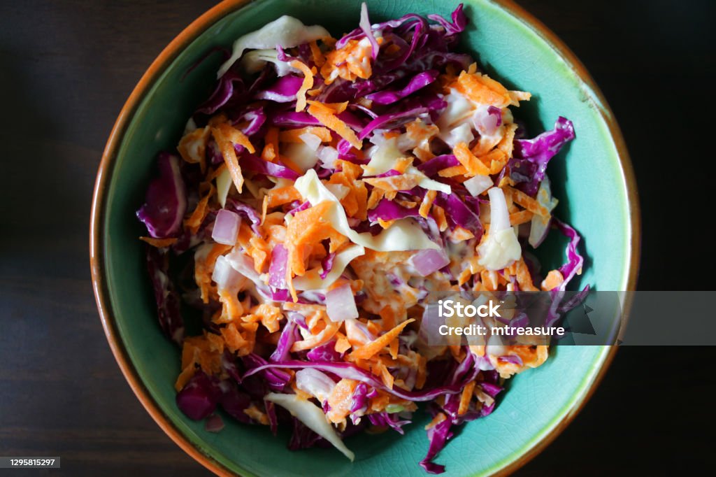 Close-up image of homemade coleslaw, shredded red cabbage, grated carrot, sliced onion, mayonnaise served in turquoise blue bowl on dark background, elevated view Photo showing elevated view of turquoise dish of homemade coleslaw, made with shredded red cabbage, grated carrot and slices of mild Spanish sliced onion, mixed with a generous amount of low-calorie mayonnaise. Coleslaw Stock Photo