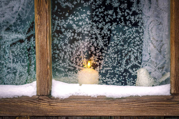 A wood-framed window, a frosty patterns. A candle burns outside the window.