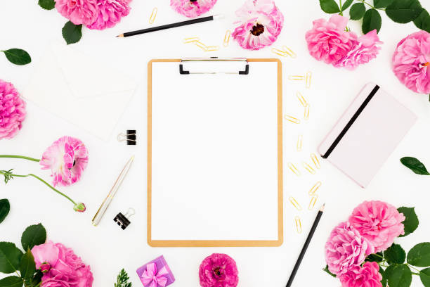istock Home workspace with clipboard, notebook, pink flowers and accessories on white background. Flat lay, top view. 1295816798