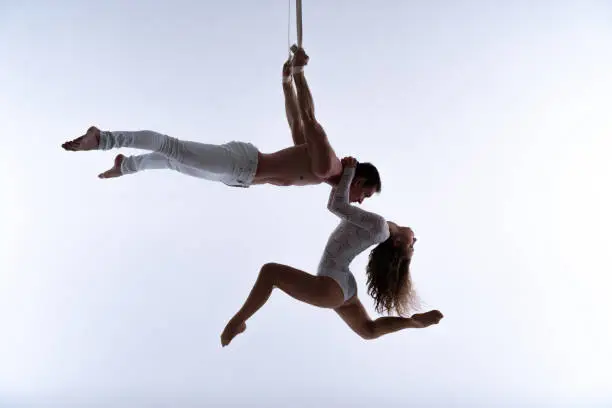 Aerial straps duo wearing white costume on white background doing performance .