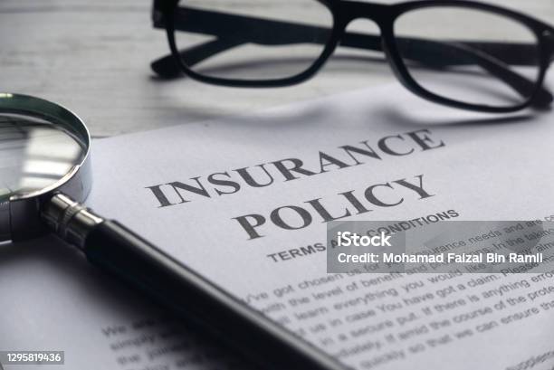 Selective Focus Of Magnifying Glassglasses And Insurance Policy Letter On A White Wooden Background Stock Photo - Download Image Now