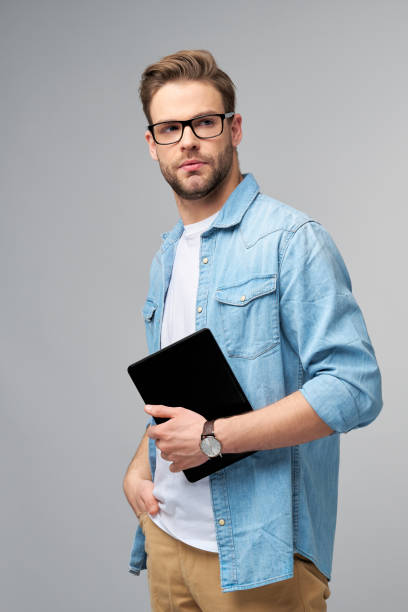 istock Happy young man wearing jeans shirt standing and using tablet over studio grey background 1295820983
