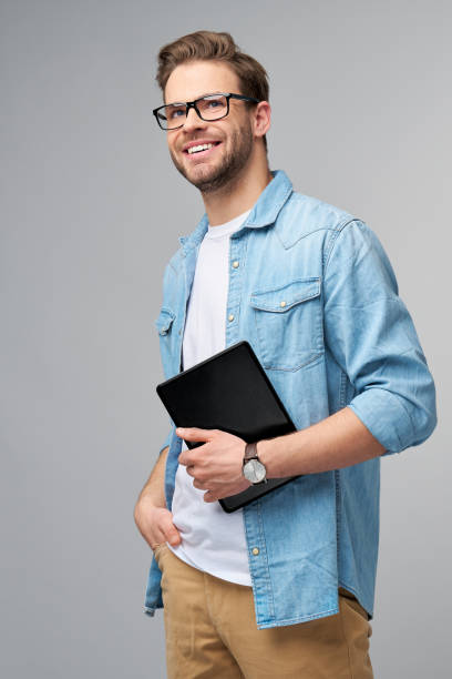 istock Happy young man wearing jeans shirt standing and using tablet over studio grey background 1295820986
