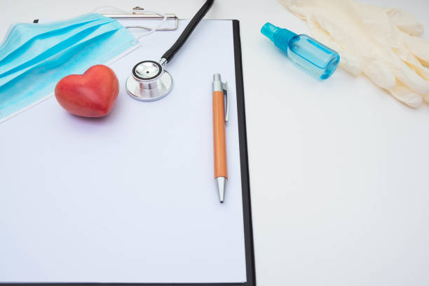 手袋、マスク、聴診器、赤い石の人工心臓、ノートシートとペンをテーブルの上の白い背景に - healthcare and medicine digital tablet medical exam doctor ストックフォトと画像