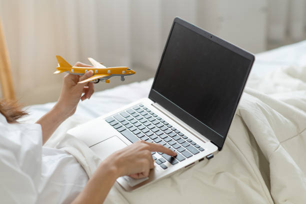 Woman hands holding model airplane and using a laptop computer, flights online booking and reservation concept