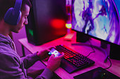 Young boy wearing headset and play video games with smartphone online in front of computer - Home isolated for coronavirus outbreak
