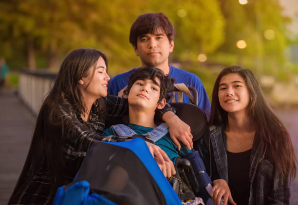 Fratello e sorelle che circondano il ragazzo disabile in sedia a rotelle al parco - foto stock