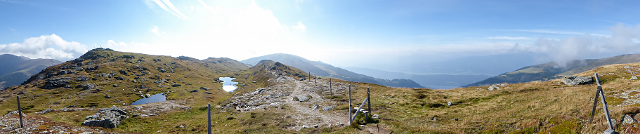 A panoramic view on the vast Austrian Alps. There is a wooden small fance along a meadow. Sunny and bright day. Endless mountain chains. Lush and vast pasture. Unspoiled landscape. Relaxation