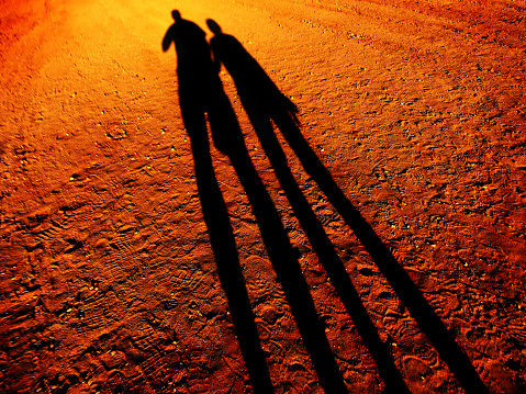 Shadow of two people holding hands walking down a dirt road together walk pathway