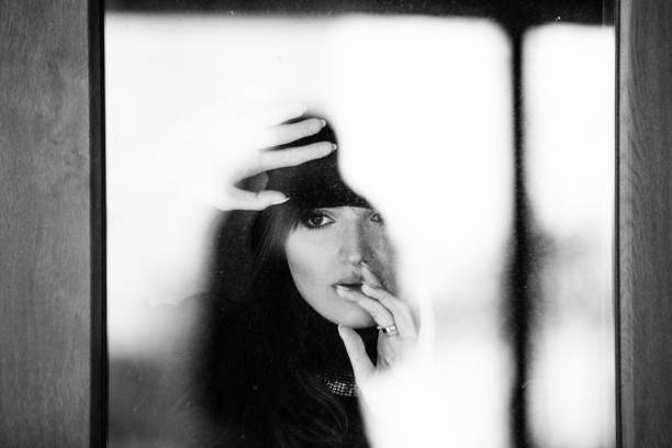 Monochrome shoot of emotional woman behind window glass looking out anxiously. Shot with DSLR Canon 5DSR and canon 70-200 F2,8 L