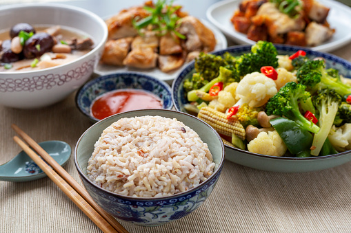 Assorted traditional chinese style meal, white rice served together with other dishes, including mixed vegetables, roasted chicken, crispy pork and lotus soup