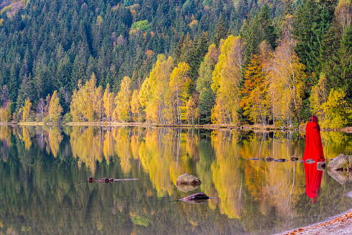 Red lady and autumn trees reflecting in water lake. Saint Anne Lake is the only one crater lake from Romania, located  in volcanic crater of Ciomatu Mare Volcano.
