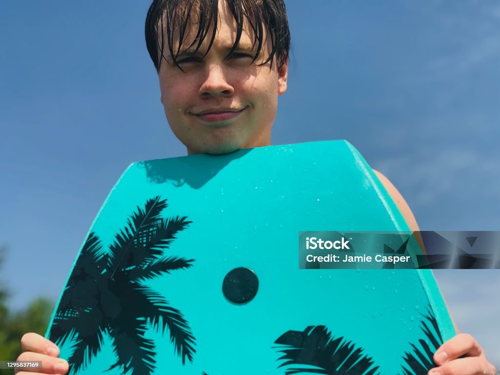 Cute smiling teenage boy at the beach. Cute smiling teenage boy, at the beach, holding part of a wakeboard near his face, he is looking at the camera and enjoying his day at the beach. Michigan Stock Photo