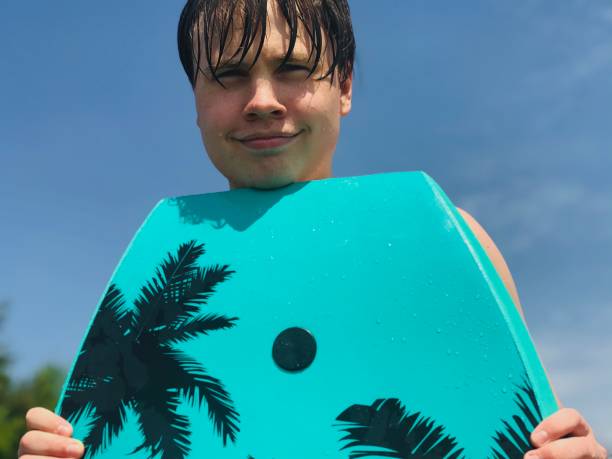 Cute smiling teenage boy at the beach. Cute smiling teenage boy, at the beach, holding part of a wakeboard near his face, he is looking at the camera and enjoying his day at the beach. gladstone michigan photos stock pictures, royalty-free photos & images