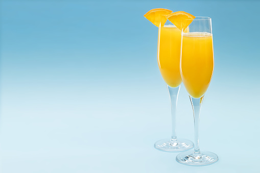 Two glasses of mimosa cocktail on blue background, copy space