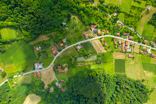 Photo was captured with a drone flying over the Zagorje region of Croatia, a short distance from the capital Zagreb. Photo shows the lush green hills and fields captured during the summer months. Shadow from a cloud is visible on the ground leaving some of the houses in the sunlight.