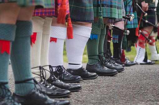 A row of Scottish bagpipers seen from the waist down show off their traditional Scottish men's attire.