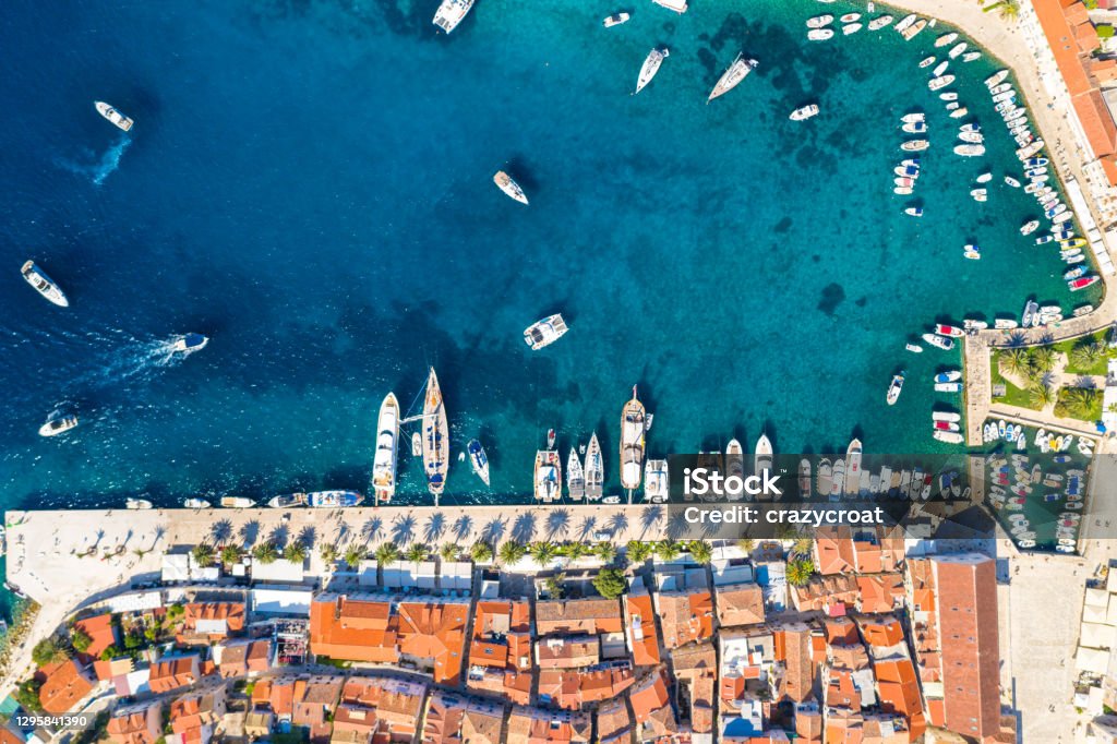 Aerial view of the harbour in Hvar town, Croatia The photo was captured in the summer of 2020 and shows the old Hvar town along with the narrow streets and wide seaside promenade. Blue water of the bay dominates the central space in the picture with ample copy room. Multiple yachts, sailing boats and small vessels are moored in the bay or tied at anchor during the busy summer months when thousands of tourists visit the island. The town was a major trading port during the medieval times when it was under the Venetian control. Hvar Stock Photo