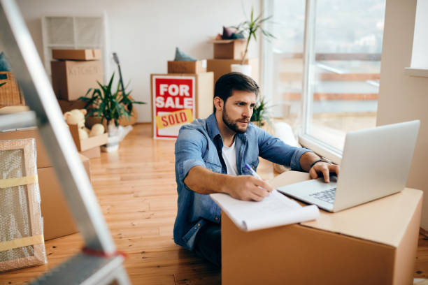 istock Mid adult man working on a computer and taking notes at his new apartment. 1295843369