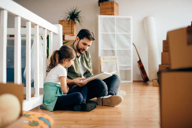 istock Father and daughter reading book while relocating in a new apartment. 1295843388