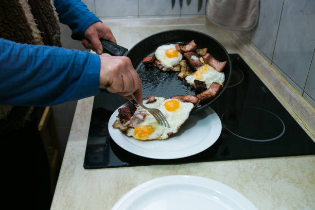 el proceso de cocción de huevos revueltos con manteca de cerdo y salchichas. el hombre prepara dos porciones. los huevos revueltos están listos. el hombre pone los huevos cocidos en los platos. - n64 fotografías e imágenes de stock