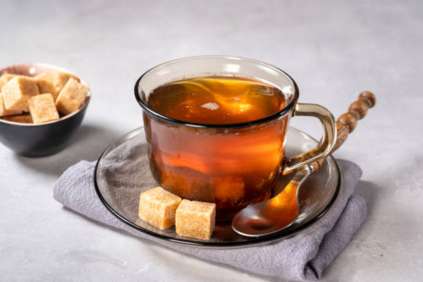 istock Glass cup of black tea with sugar cubes on light background 1295845220
