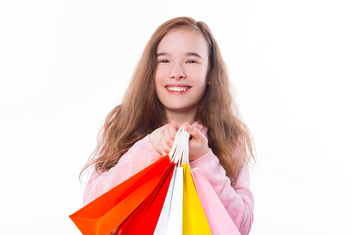 Close up portrait of smiling little girl holding shopping bags over white background.