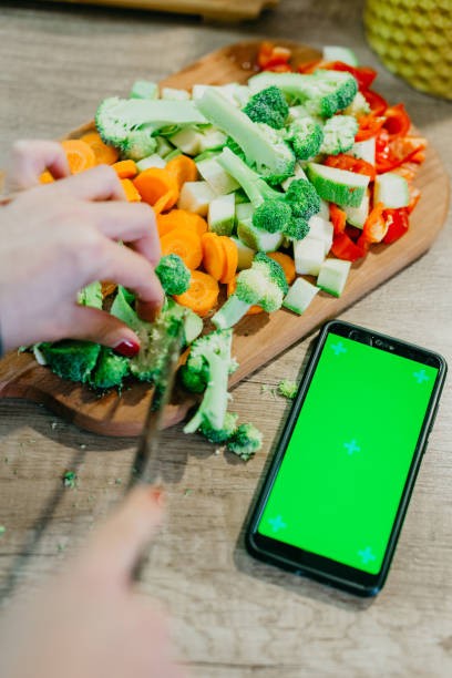 istock Hand cutting veggies and mobile device next to it 1295846147