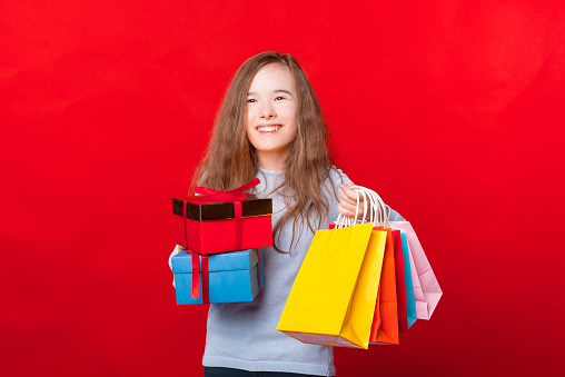 Happy child holding two gift boxes and many colorful shopping bags and looking away.