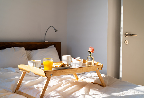 Breakfast in bed on tray at sunny morning at home - orange juice, coffee, toasts, flower. Happy Mother's day.