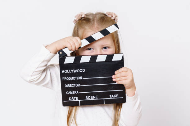 istock A girl looks through a clapperboard into the camera. Isolated over white background. 1295854511