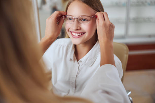 istock Beautiful friendly young lady looking ahead while unrecognized woman helping to choose glass in room indoors 1295856335
