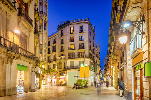 Pedestrian shopping street with stores in old town Gothic Quarter, downtown Barcelona, Catalonia, Spain at twilight blue hour.