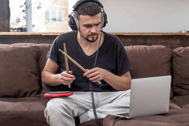istock A young man with headphones learns to play the drum using online lessons. 1295858504