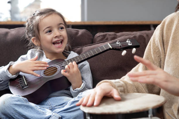 милая маленькая девочка учится играть на укулеле дома. - 20s acoustic guitar adult attractive female стоковые фото и изображения