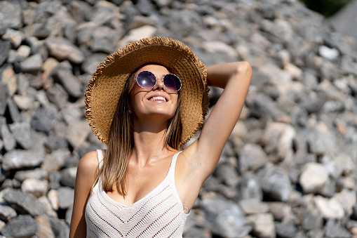 Beautiful smiling young woman with sun hat and eyeglasses posing outdoors on sunny day