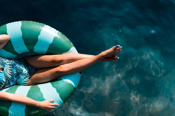 belle donne che si rilassano in piscina mentre sono sedute su un anello gonfiabile - swimwear women swimming pool people foto e immagini stock