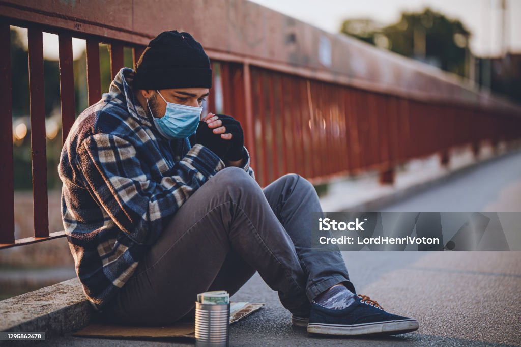Homeless person sitting on the bridge with donation can Homeless person wearing protective mask and sitting on the bridge with donation can Homelessness Stock Photo