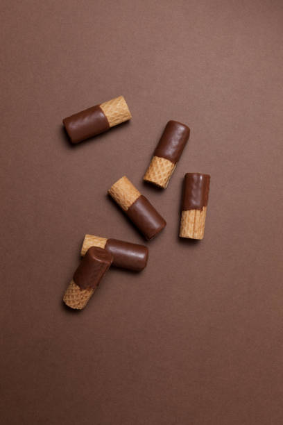 istock Crispy wafer rolls half-coated in milk chocolate. Top view, brown background, copy space 1295866826