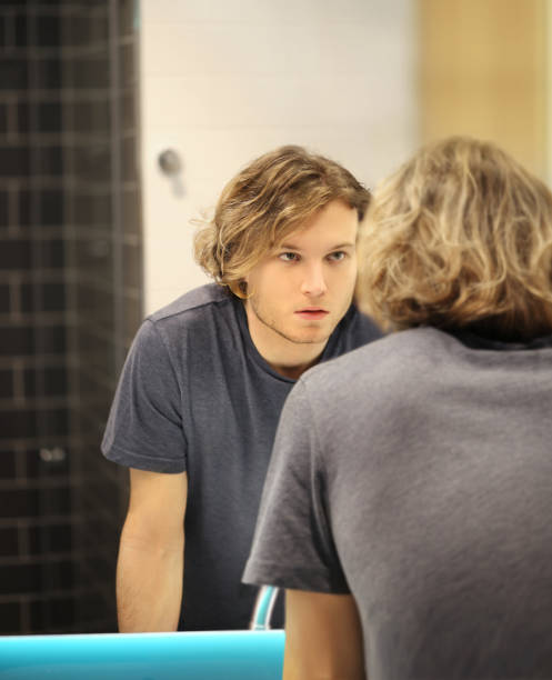 istock young man looking in the mirror,combing his hair,looking at problems on face 1295867773