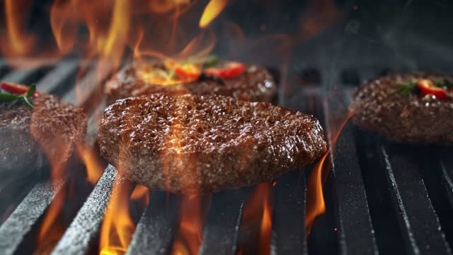 Barbecued Beef Burger Patty Falling onto Smoking and Flaming Grill Grate in Slow Motion