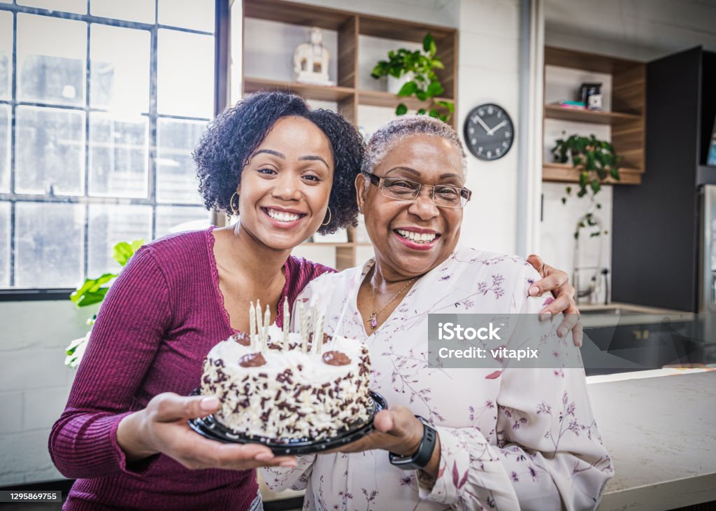 Celebrating Grandma's Birthday Granddaughter presenting a cake to her grandmother. Birthday Stock Photo