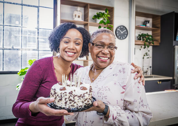 Celebrating Grandma's Birthday Granddaughter presenting a cake to her grandmother. 70s birthday party cake stock pictures, royalty-free photos & images