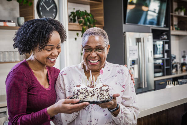 Celebrating Grandma's Birthday Granddaughter presenting a cake to her grandmother. 70s birthday party cake stock pictures, royalty-free photos & images