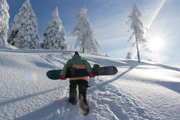 snowboarder haciendo senderismo por la montaña llevando una tabla de snowboard - snowboard non urban scene woods snowboarding fotografías e imágenes de stock