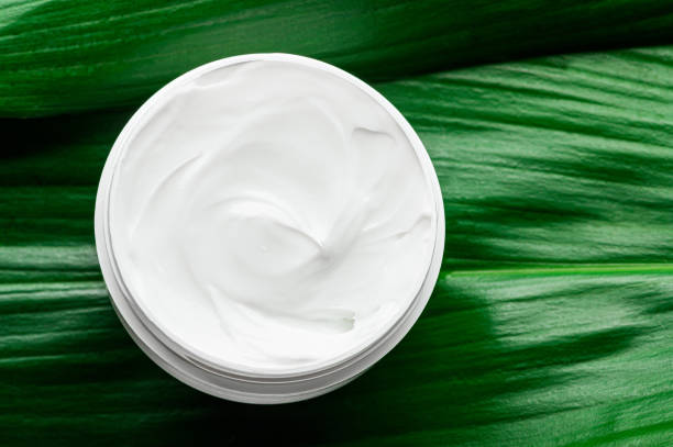 istock Moisturizing white cream in plastic jar on greenery top view. Organic cosmetics for moisturizing and nourishing the skin of the face, hands. Body creme with natural ingredients,eco-friendly packaging 1295877205